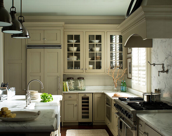 Una cocina de estilo rústico con gabinetes pintados de color verde grisáceo y encimeras de mármol.