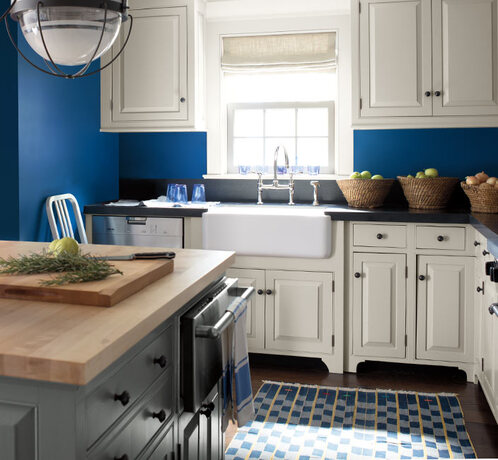 A blue-painted kitchen with white cabinets, a butcher block countertop island and white farmhouse si
