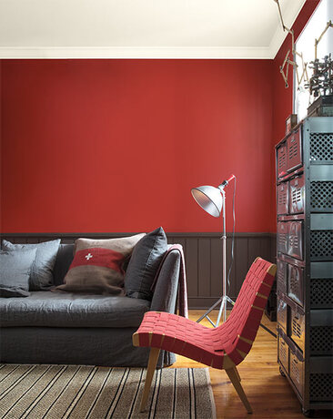 A red living room with brown wainscoting and a contemporary red woven chair.