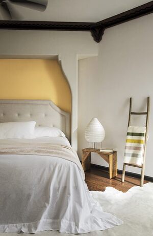 Off white walls with a yellow accent wall behind a tan bedframe with gray bedding.