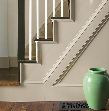 A sideview of white-painted stairs with white spindles and black handrail.