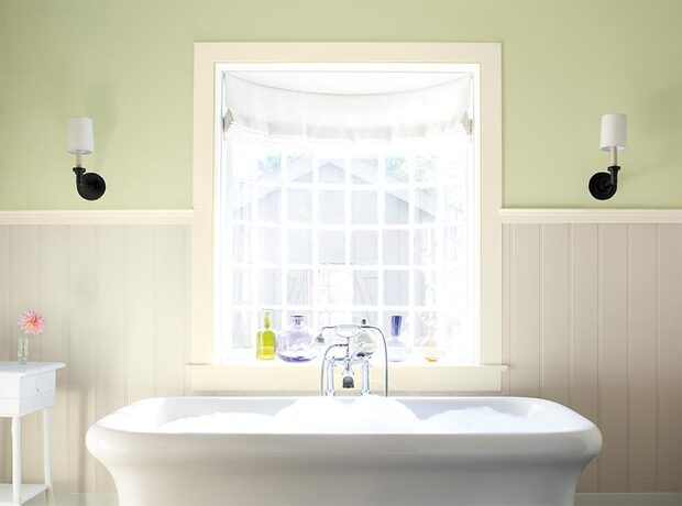 A light green-painted bathroom, detailed with white wainscoting and a stand alone tub.