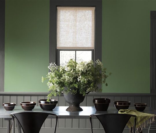 Green painted walls lightens this dining room with dark gray trim, wainscoting and table.