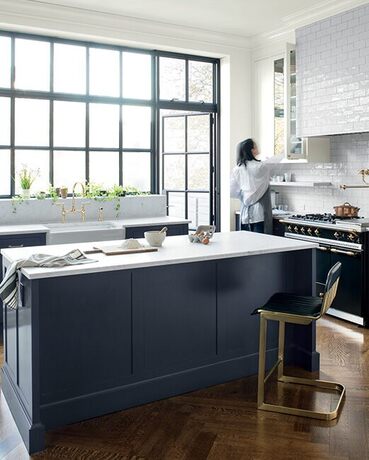 A navy blue kitchen island with white marble countertops in an open kitchen with large windows