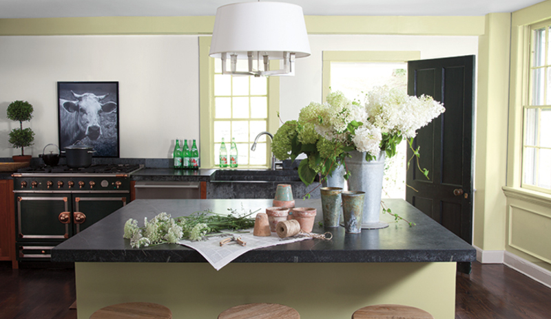Una moderna cocina pintada de verde con flores cortadas y encimeras de granito.