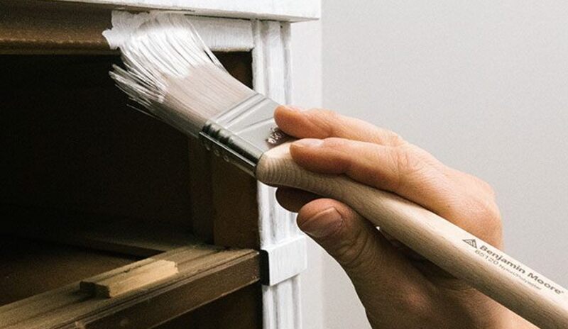 Aplicando imprimación en la superficie de un armario en una habitación con paredes blancas.