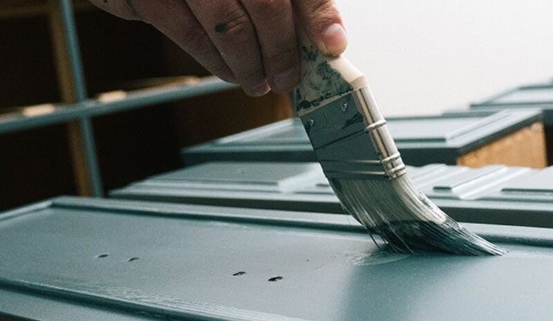 Primer is applied to the surface of a cabinet in a room with white walls.