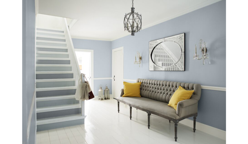 Área de estar azul-gris con escaleras de dos tonos, sofá gris y cojines amarillos, lámpara de araña