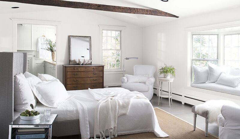 Acogedora habitación blanca con ropa de cama, sillas, ventana de bahía, cómoda antigua, techo