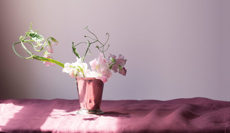 Una tela sobre una mesa, rematada con una maceta de flores frente a una pared violeta Porcelana